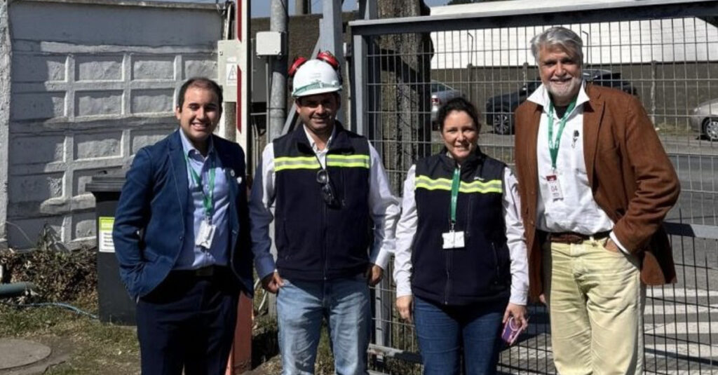 Quatre personnes debout devant une clôture, souriant.